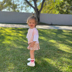 Child standing on grass with a white fence and trees in the background