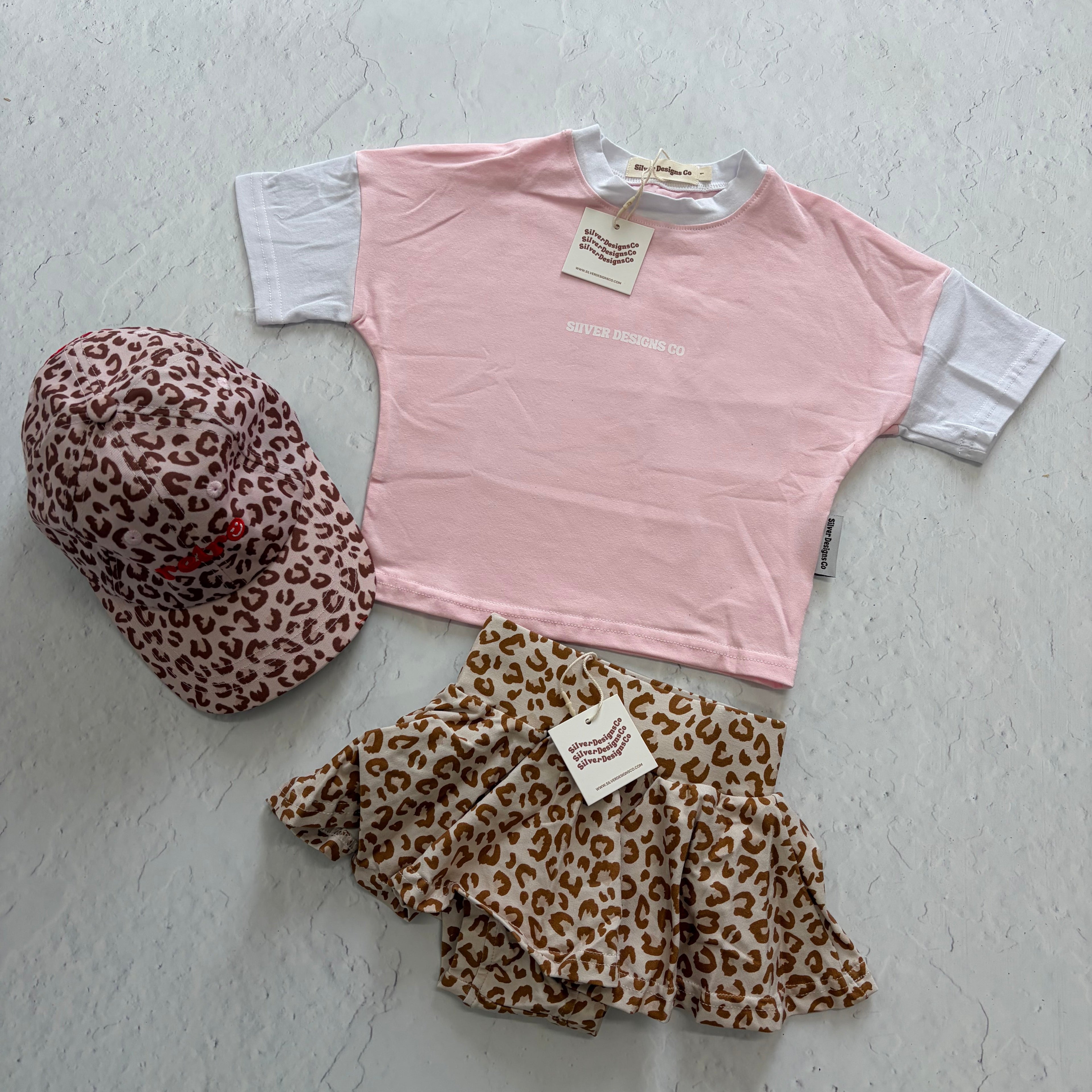 Pink t-shirt with leopard print shorts and headband on a light gray surface